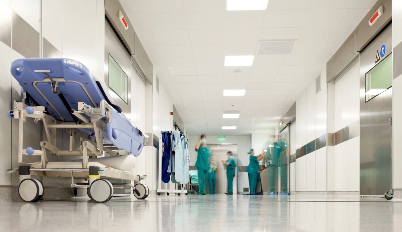 image of hospital hallway with hospital bed and people in scrubs in the distance