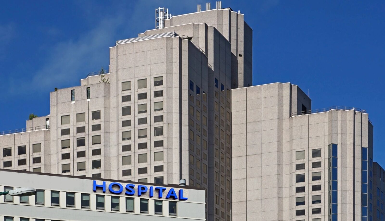 tall white facade buildings against a blue sky; one building has the word hospital in blue letters