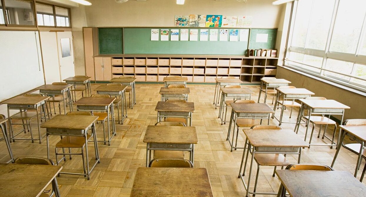 empty old style classroom with wooden desks, wood floor, and green blackboard