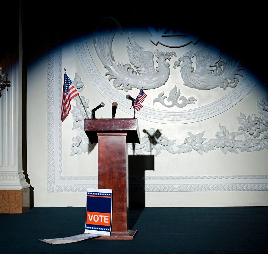 image of empty lectern with American flags and a "Vote" placard